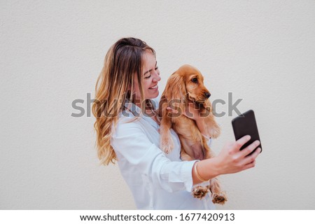 young woman at the street with her cocker dog taking a picture with mobile phone. Lifestyle outdoors with pets