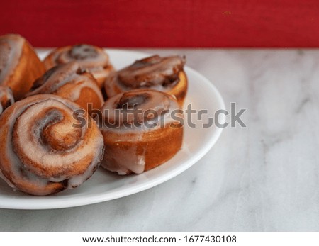 Side view of bite size cinnamon swirl rolls on a white plate atop a marble tabletop with a red wall in the background illuminated with window light. Royalty-Free Stock Photo #1677430108