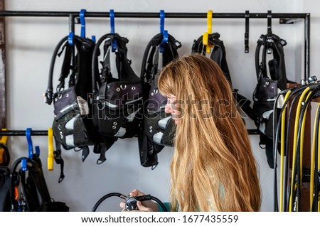 Girl dressing up with scuba diver's equipment. young Caucasian girl prepares equipment for diving, checks the oxygen tank, and holds the regulator in her hands.