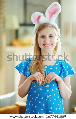 Portrait of cute modern little princess in a polka dot blue overall and easter bunny ears at modern home in sunny spring day.