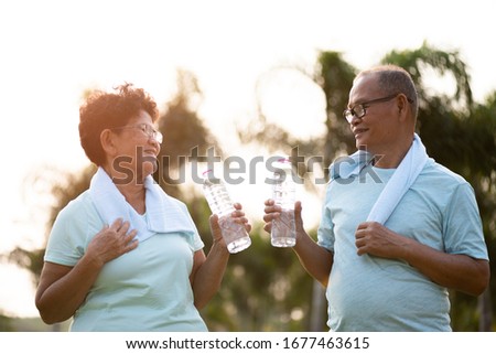 A couple of asian old man and woman doing physical exercise outdoor and holding plastic bottle drinking water. Be healthy and strong. Senior healthcare and sport concept.