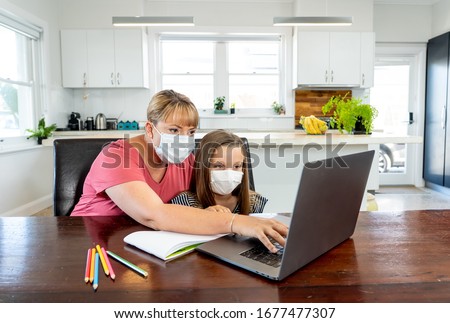 Coronavirus Outbreak. Lockdown and school closures. Mother helping bored daughter with face mask studying online classes at home. COVID-19 pandemic forces children and teachers online learning. Royalty-Free Stock Photo #1677477307