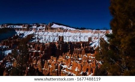 Long exposure shot during a bright full super moon at the famous natural amphitheater located in Bryce Canyon National Park, Utah with pillar shaped red rock and snow on a clear night.