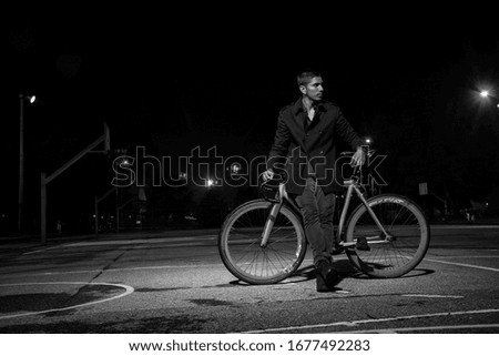 Black and white picture which is a young man lying on his bike in a dark park at night