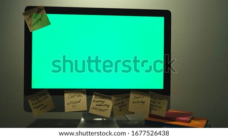 Stylish and creative desk with computer green screen and many sticky notes, office accessories. Concept. Close up of a woman hand taking one post it note from the computer with chromakey.