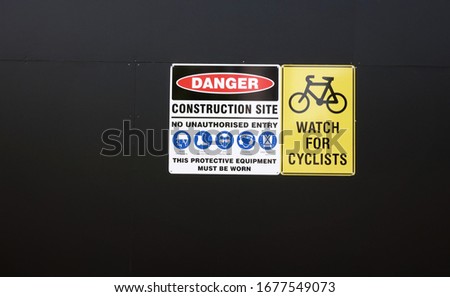 Warning sign with symbols on black wall. Danger construction site, no unauthorised entry. Protective equipment must be worn. Head foot eye hearing protection. High visibility vest. Watch for cyclists.