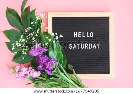 Hello Saturday text on black letter board and bouquet colorful flowers on pink background. Concept Happy Saturday. Template for postcard, greeting card Flat lay Top view.