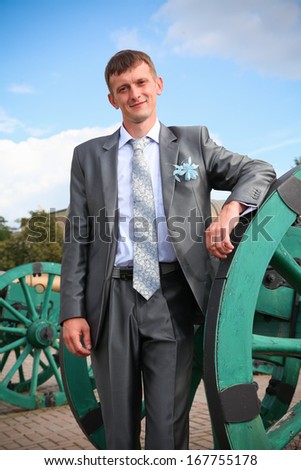 Handsome man in suit leaning against old cannon at castle