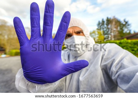 Man wearing protective mask and hazmat suit against the Coronavirus Covid-19 epidemic and doing a warning stop sign with his hand during lockdown and quarantine. Scared and angry looking professional