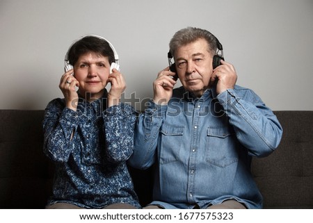A couple listening to music together in wireless headphones. An older man and a woman enjoying music as a hobby. Staying at home during COVID-19 pandemic and enjoying hobbies.