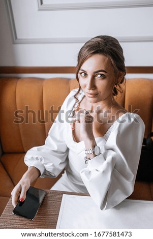 A young beautiful woman is sitting in a cafe and holding a phone in her hands and looking at the camera. close- up, brown photo processing