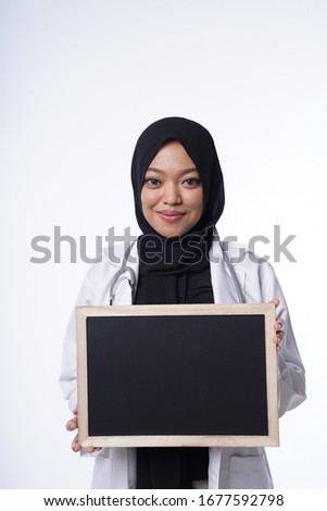 Portrait of young female hijab doctor wearing a stethoscope while holding a tiny chalkboard.