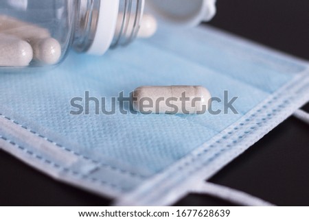 Surgical mask and few tablets with container lies on black background. Mask should protect against viruses and pills increase the immune system.