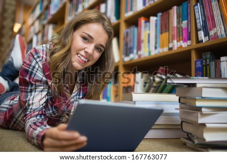 Young smiling student lying on library floor using tablet in college