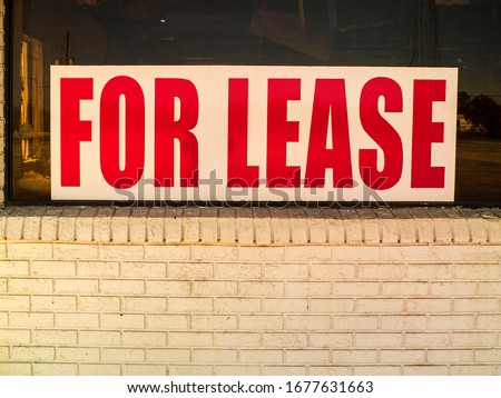 For Lease Red Letters with White Background on the Front Window of an empty Store. Empty Storefront with a For Lease Sing on the Window.