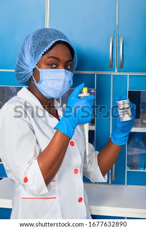 Portrait of African female medical student, woman scientist In white gown, plastic hat, gloves, mask holds pipette and test for pcr nucleic acid dna korona virus, diagnostics of covid-19 in patients.