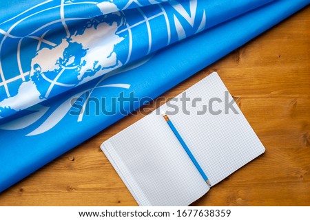 Close-up of the UN blue flag with the image of the countries of the participants with a notepad lying on a wooden table. International politics concept