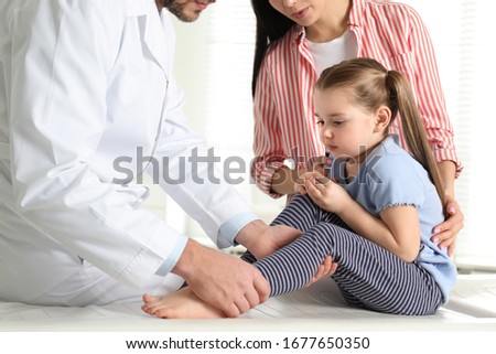 Professional orthopedist examining little patient's leg in clinic