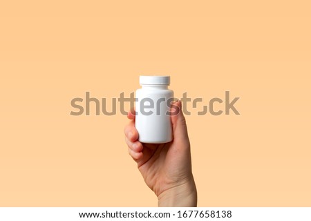 Viral disease prevention concept. Female hand holds jar with vitamins, pills, medicines or drugs on orange background. Coronavirus prevention. Safety rules during quarantine. Copy space for text Royalty-Free Stock Photo #1677658138