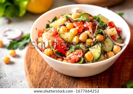 Chickpea salad with tomatoes, cucumber, feta cheese, parsley, onions and lemon in a plate on a served table, selective focus. Tasty and healthy vegetarian food, oriental and Mediterranean cuisine. Royalty-Free Stock Photo #1677664252