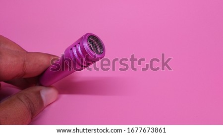 mini mic used for karaoke held by hand, isolated with a pink background