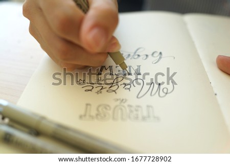 Selective focus image of female hand writing with pen. Creative handwriting calligraphy alphabet.