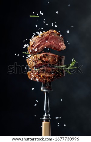 Grilled beef steak with spices on a black background. Beef steak on a fork sprinkled with rosemary and sea salt.    Royalty-Free Stock Photo #1677730996
