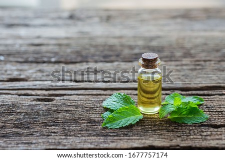 Essential oil of peppermint in a small bottle with fresh green mint on an old wooden background, selective focus