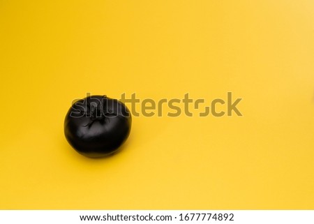 Matte black tomato on the yellow background. The object is at the left side of the picture. Minimal style. Conceptual minimalism. Fruit. One. Copy space