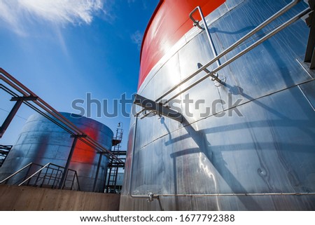 Orange and metallic steel storage tanks with acid. at sulfuric (sulphuric) acid plant. On blue sky background. Wide-angle view. Royalty-Free Stock Photo #1677792388