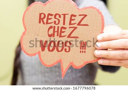 closeup woman hand holding speech card bubble with french word restez chez vous translated in english stay at home 