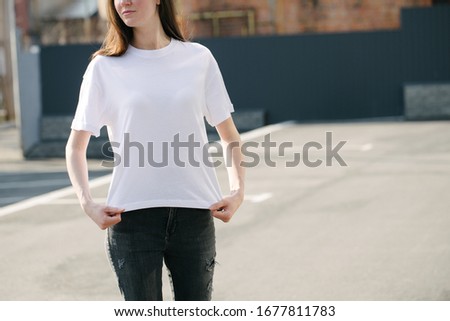 Skinny woman wearing white blank t-shirt and black jeans with space for your logo or design in casual urban style over city street background