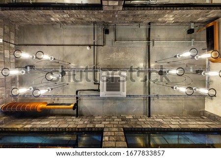 looking up on gray concrete ceiling with halogen spots and edison lamps in loft office room with air conditioning and orange ventilation pipe
