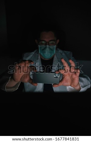 Stock photography of doctor taking screen photography. He wears a white coat and a protective mask. Photography from front view.
