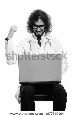 Studio shot of happy man doctor smiling while using laptop with fist raised