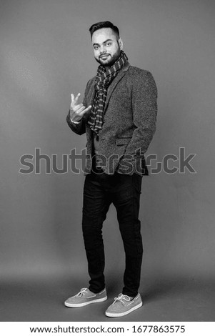 Young bearded Indian businessman against gray background