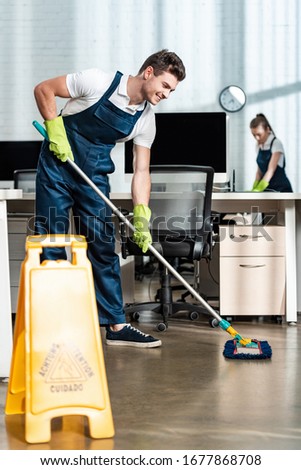 smiling cleaner washing floor with mop near colleague cleaning desk