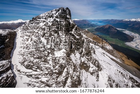Massif mountain summit with snow, lake and hills in background. Peak close Glenorchy aerial drone photo. Beautiful valley with river formations, highlands, hills with forest, trees and Lake Wakatipu.