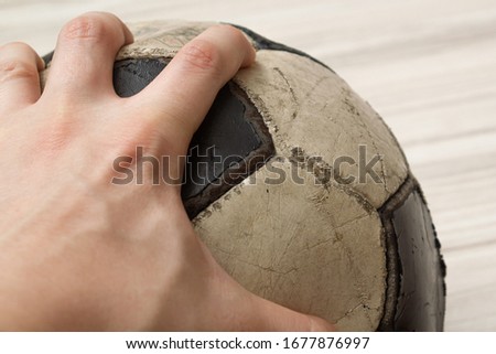 old beaten shabby soccer ball with hand on it on a background of light wood