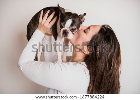 A woman with is Boston Terrier on studio white background