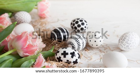 Top view beautiful golden and black-white modern easter eggs lie on a white wooden table next to hay and pink fringed tulips. Stylish easter concept. Spring card. Copyspace