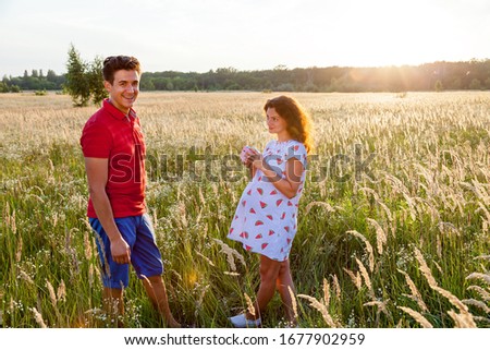 A beautiful outdoor image of a young man giving a present to his pregnant wife.Pregnant family photo shoot in nature
