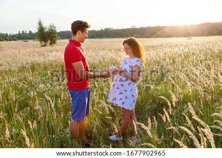 A beautiful outdoor image of a young man giving a present to his pregnant wife.Pregnant family photo shoot in nature