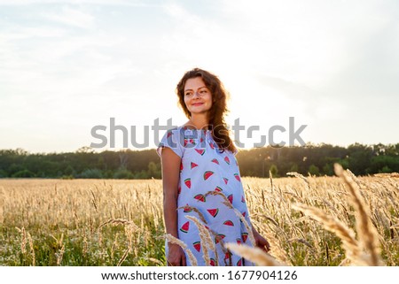 A cute pregnant woman in a beautiful dress is standing in the wheat field at a sunset.Pregnant family photo shoot in nature