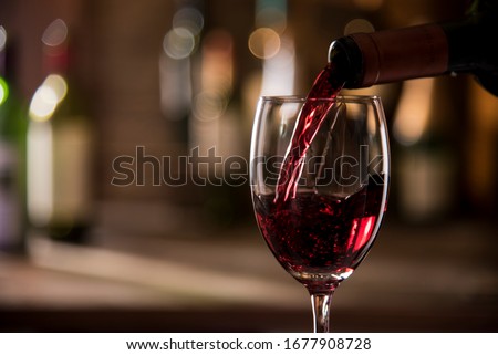 pouring red wine from bottle into glass bokeh background