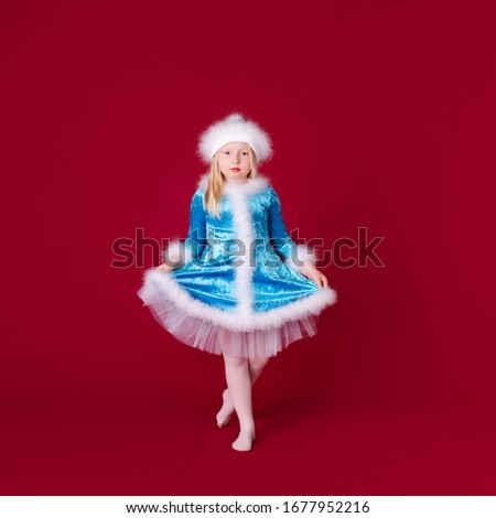Little blonde girl in a christmas and new year Santa costume having fun and sending kisses on red background. Space for text. Dreams come true Merry Christmas.