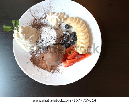 Desserts in a white plate, ice cream, banana, chocolate, whipped cream, strawberry on the table.