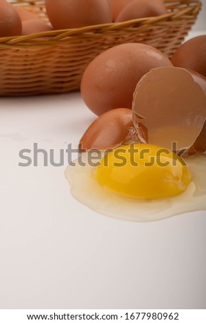 A broken chicken egg, chicken eggs in a wicker basket and chicken eggs scattered on a white background. Close up.