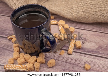 Dark blue ceramic tea mug, cookie sticks with white icing and chocolate and brown cane sugar pieces on a wooden background. Close up.