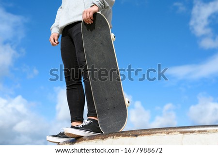 Close up of unrecognizable young man holding skateboard in the park on blue sky background .